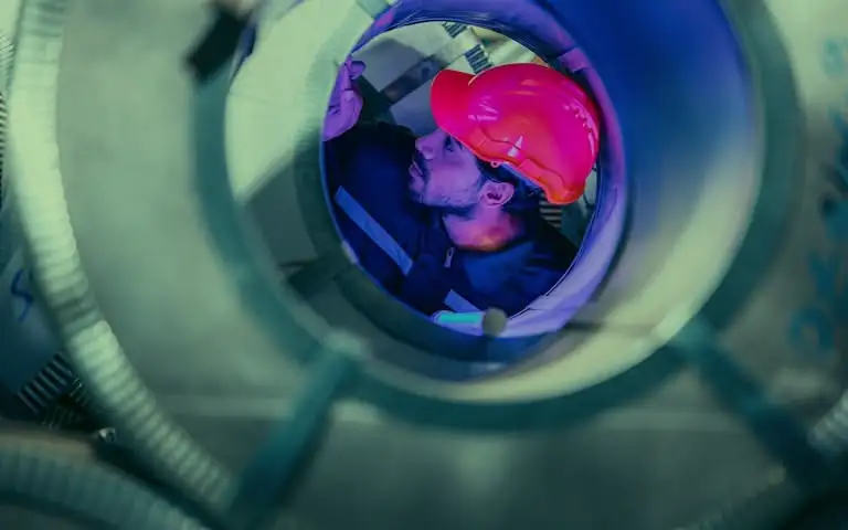 Homme inspectant tube métallique, casque rouge.